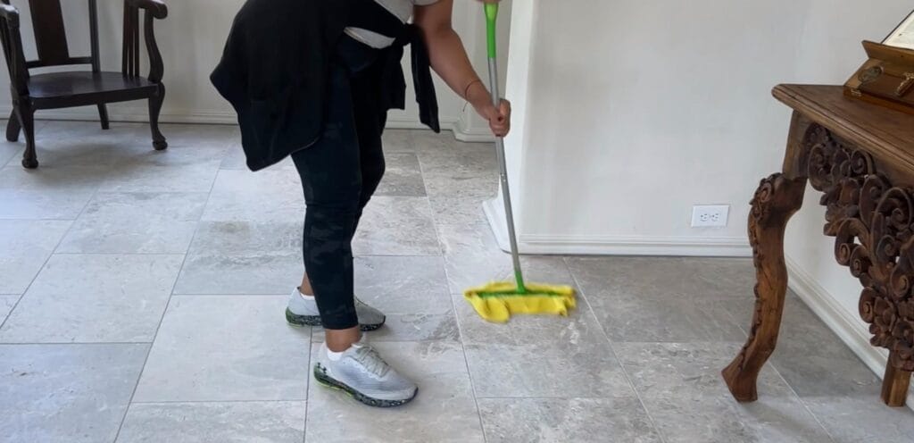 Residential cleaning in Georgia: Person mopping a light-colored tile floor in a room with minimal furniture.
