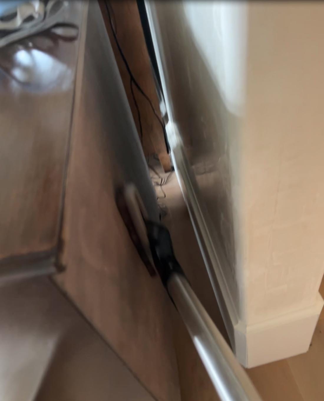 A vacuum cleaner wand is being used to clean dust between a wooden cabinet and a white wall.