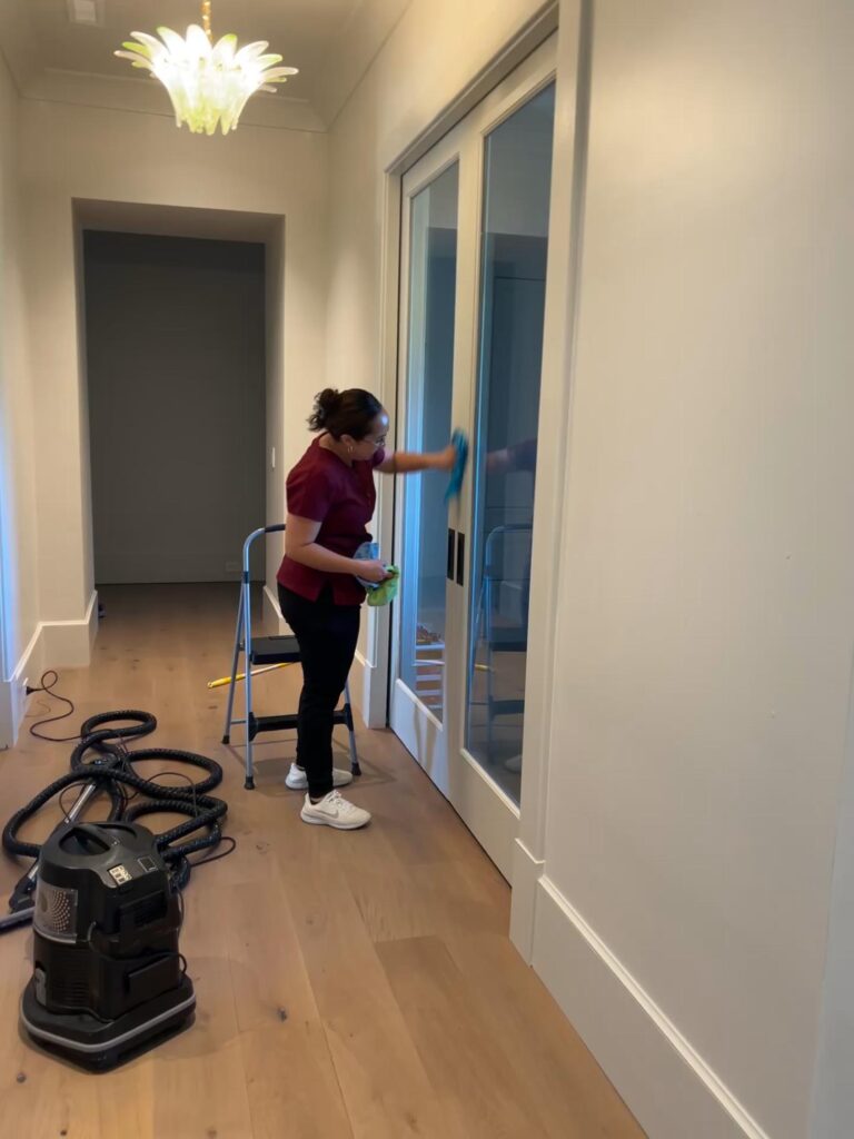 Professional cleaner meticulously cleans glass doors in a modern home, perfect for detailed move-in move-out cleaning services. Ensure your new or old space sparkles.
